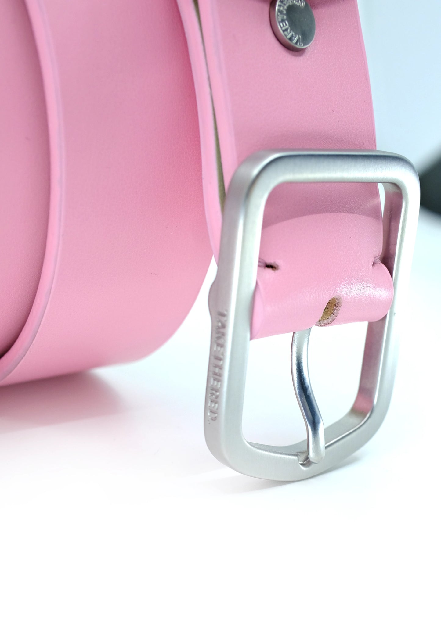 Close-up of Barbie Pink leather belt with a weathered silver buckle and "BIRD & ASH." engraved on the side.