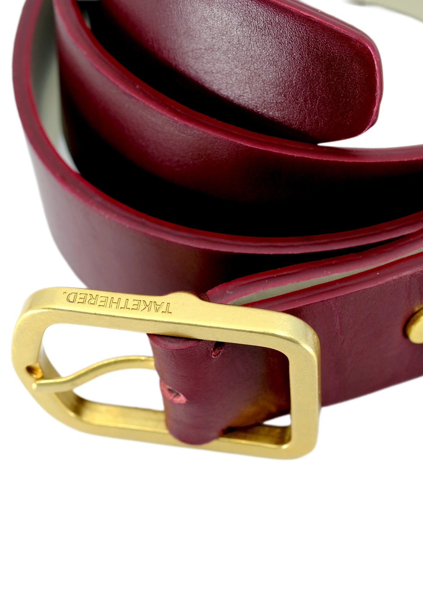 Close-up of Classic Red Mist burgundy leather belt with a matte gold buckle and engraved "BIRD & ASH." logo.