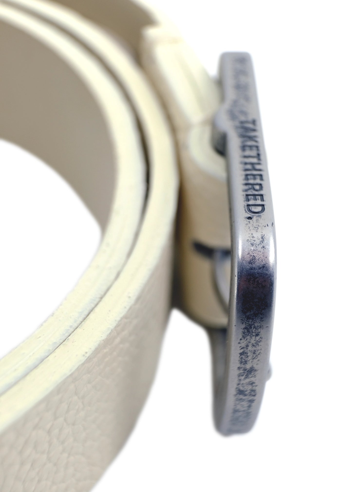 Side view of an off-white belt showing a weathered silver buckle engraved with the brand name "TAKETHERED."