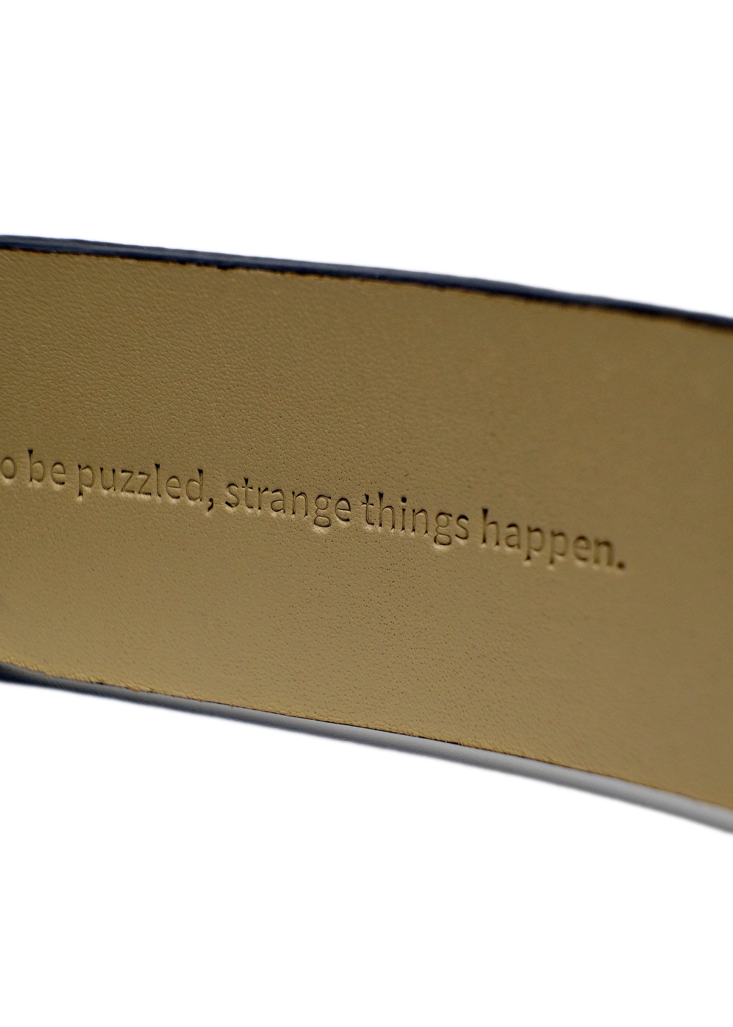 Close-up of the tan belt interior with the embossed hidden text "to be puzzled, strange things happen."