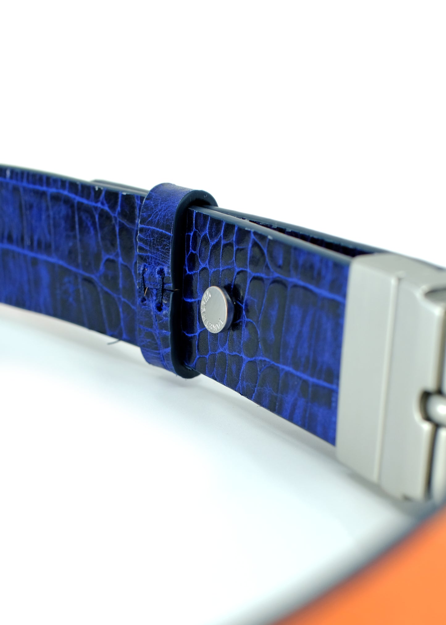 Close-up of Shadow Blue crocodile embossed leather with a silver-tone rivet and a glimpse of the orange interior.