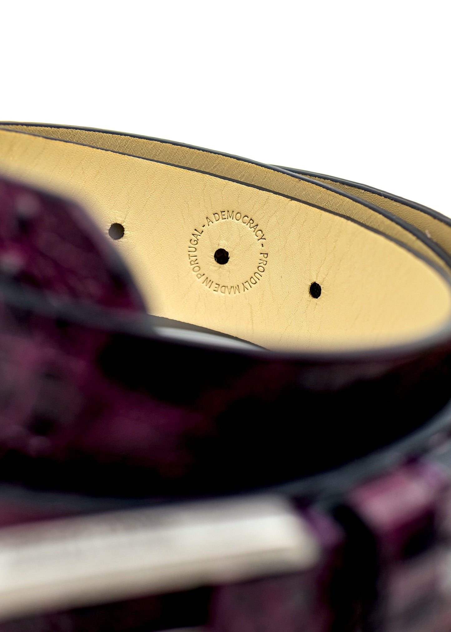 Close-up of Dirty Aubergine belt interior with "Proudly Made in Portugal" circular stamp on cream leather.