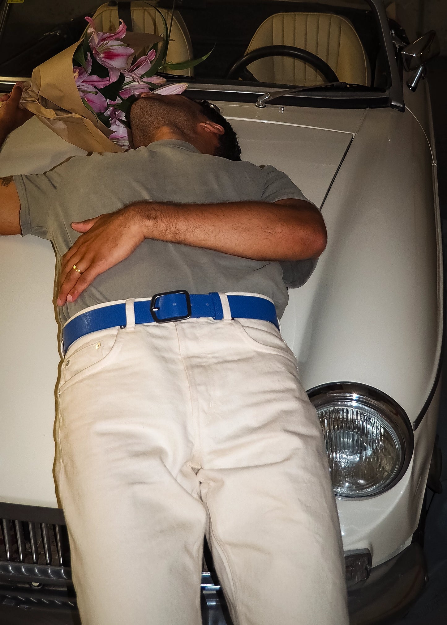 Lifestyle shot of Betty Blue Grunge Belt worn with white jeans by a man leaning against a classic white car.