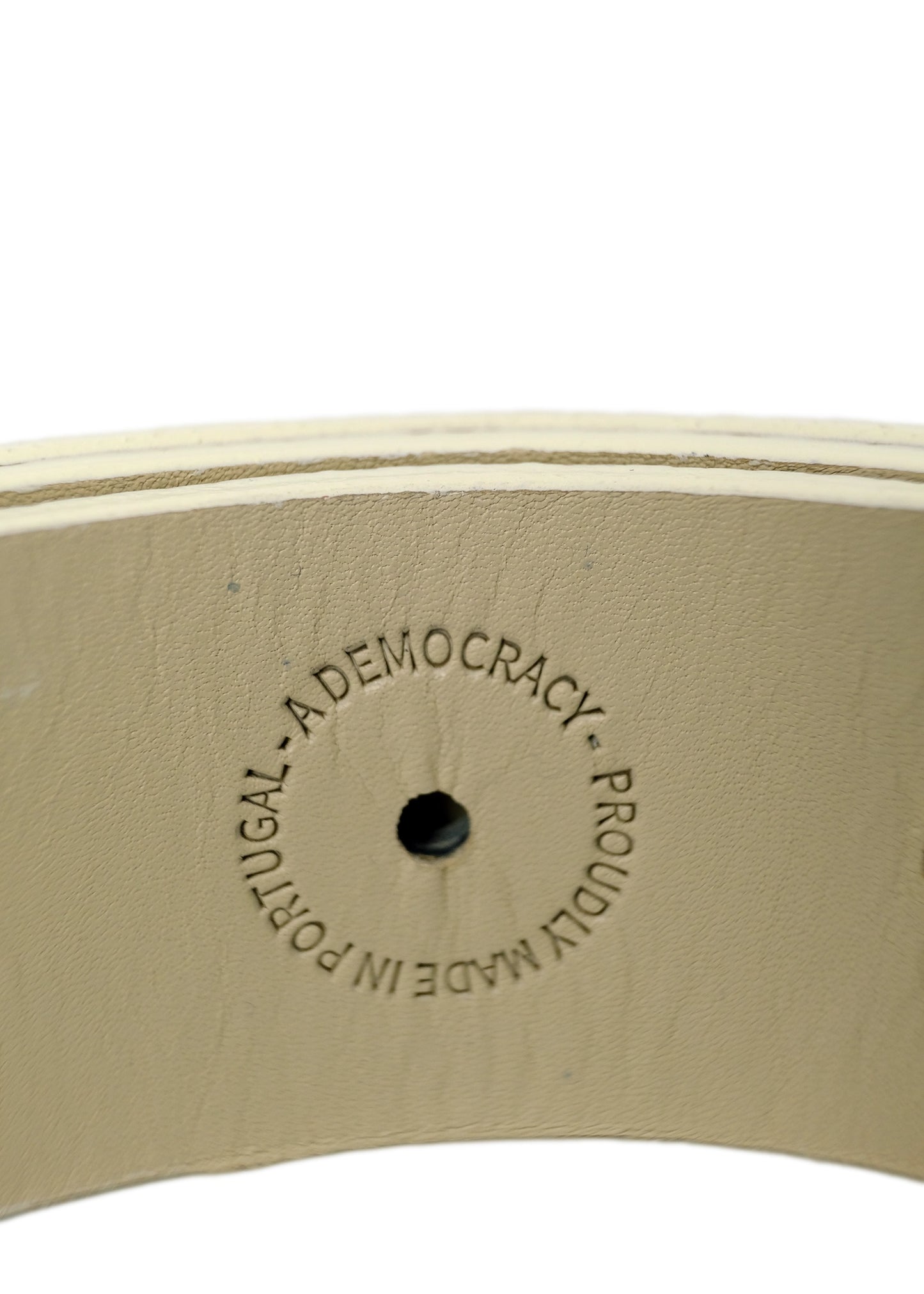 Close-up of an off-white belt interior featuring a "PROUDLY MADE IN PORTUGAL - A DEMOCRACY" embossed stamp.