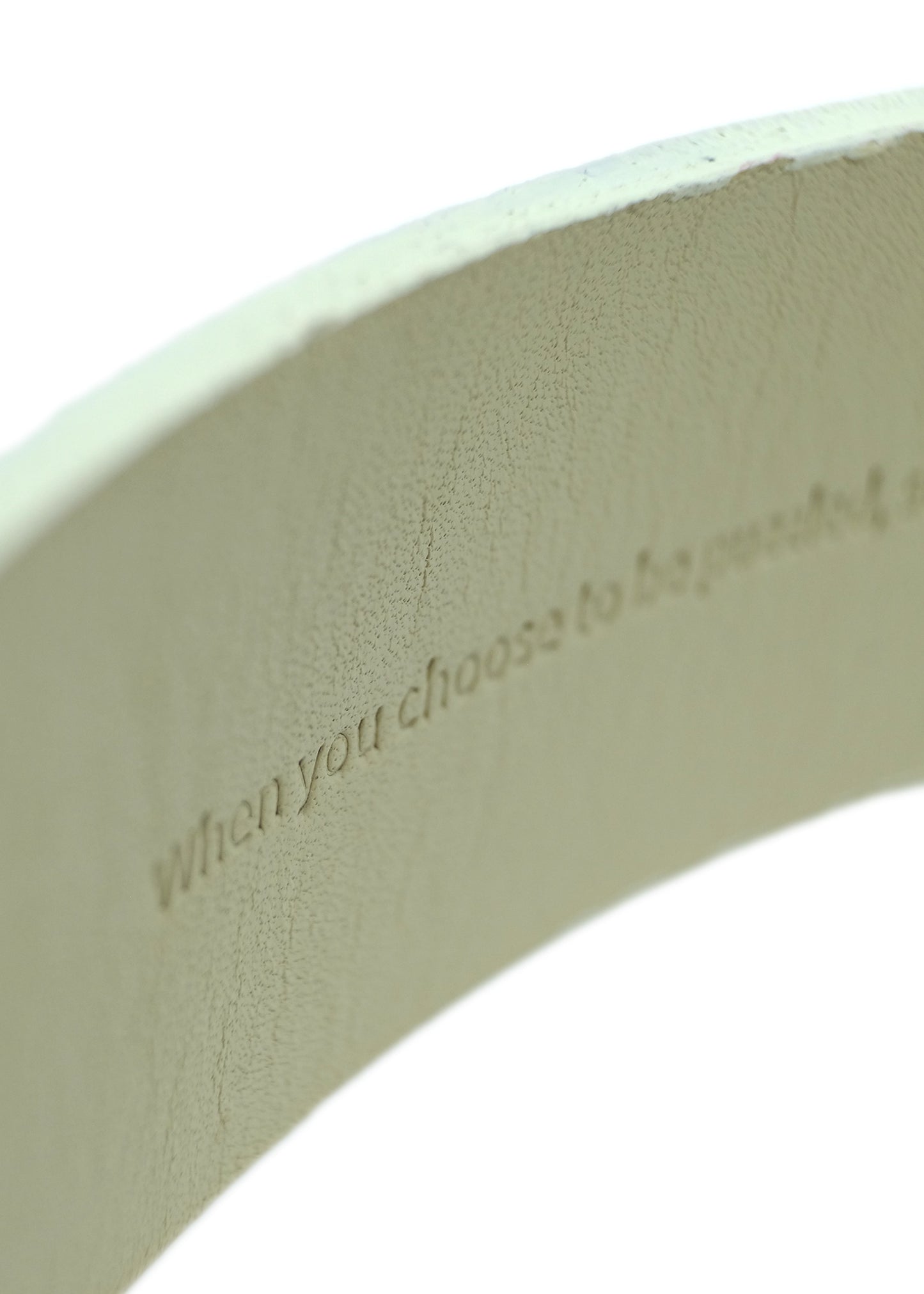Interior view of an off-white belt showing the hidden embossed text: "When you choose to be puzzled..."