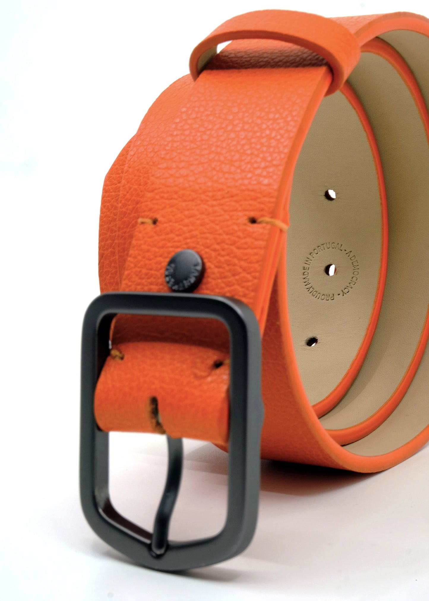 Close-up of coiled orange Tatooine Sunset Grunge Belt showing a matte black buckle and a "MADE IN PORTUGAL" interior stamp.