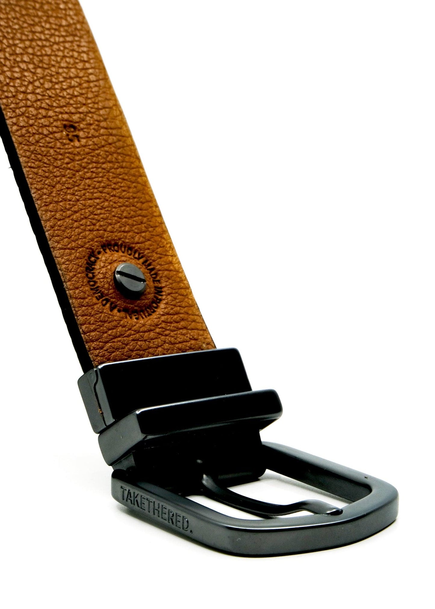 Close-up of a matte black reversible buckle on a Smokey Cognac-grained leather belt with "BIRD & ASH." engraving.
