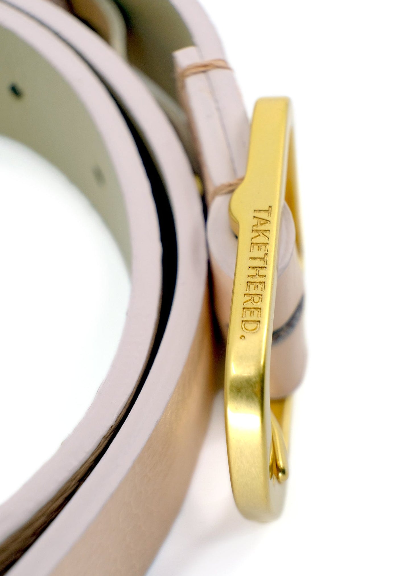 Side view close-up of a gold buckle engraved with "BIRD & ASH." on a Nude Pink pebble-grain leather belt.