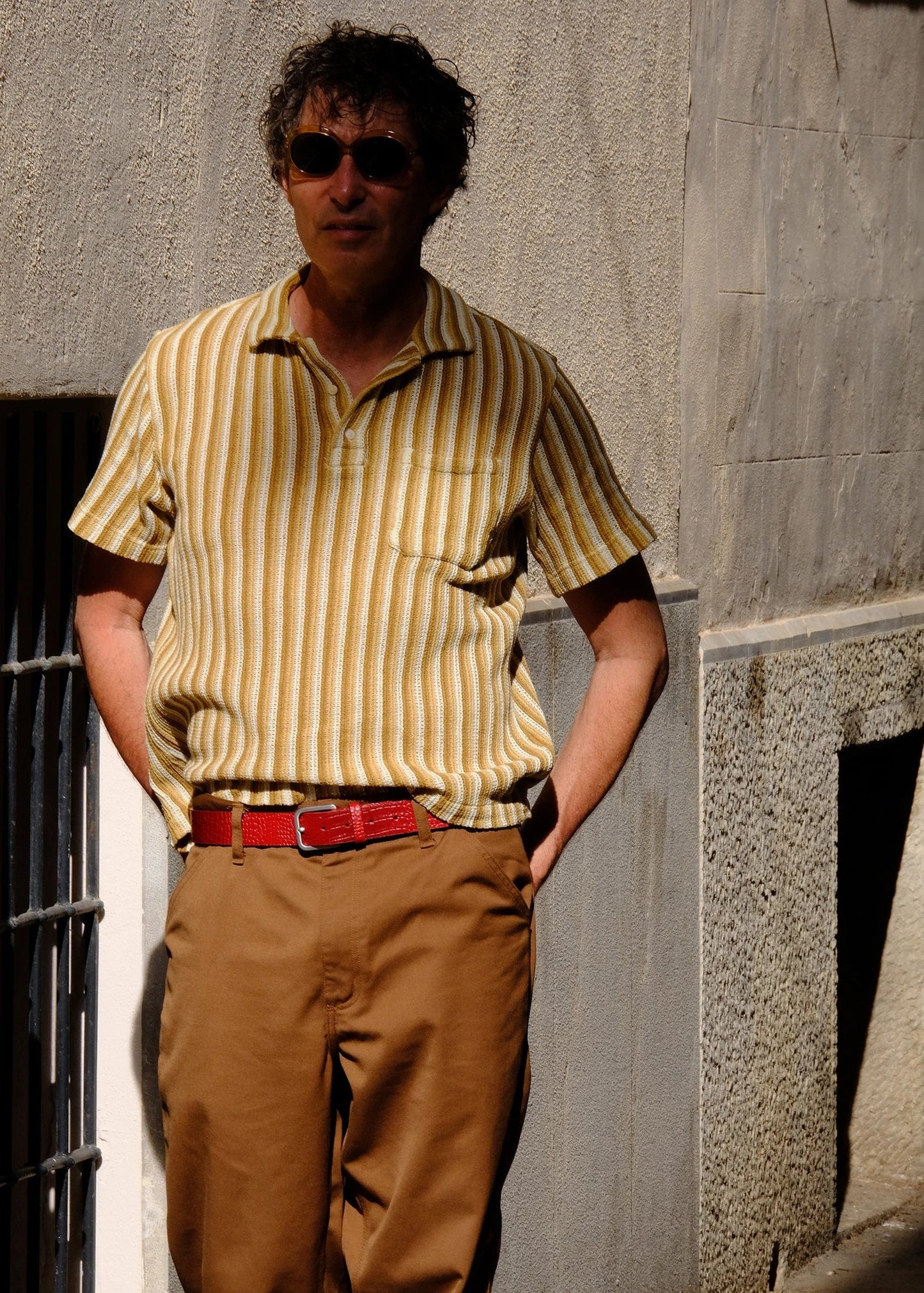 Lifestyle shot of the red alligator-embossed Blood Simple belt worn with brown trousers and a yellow striped shirt.